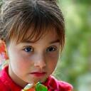 A young girl intently examining a leaf through a magnifying glass.
